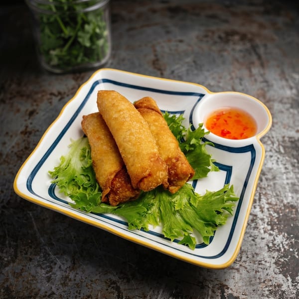 Three golden-brown spring rolls on a bed of lettuce, with a side of sweet chili sauce.